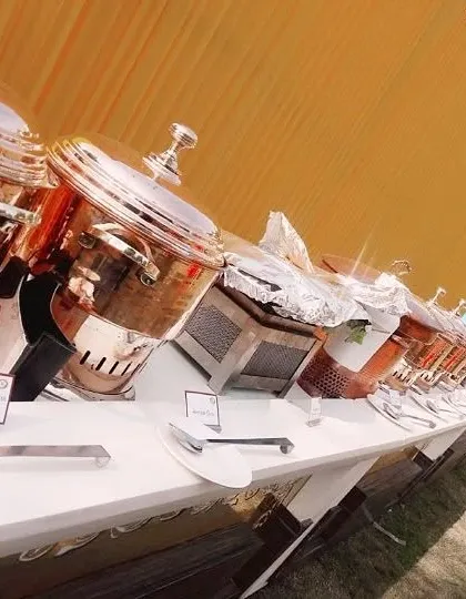 A close-up of our buffet line, showing a row of gleaming copper and silver chafing dishes ready for service at an outdoor event.