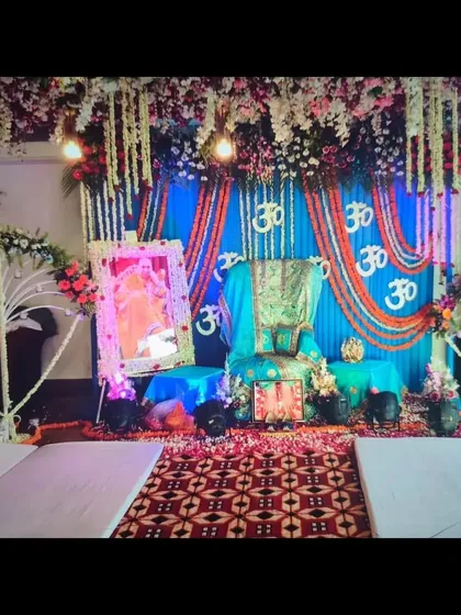 A full view of the blue themed Guruji Satsang decoration. You can see the floral canopy, the Om symbols on the backdrop, and the seating arrangement in front of the stage.
