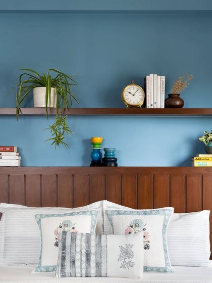 This master bedroom is a serene and stylish retreat. The headboard provides both back support and hidden storage, while sleek ledges above the bed offer space for plants and personal mementos against a calming blue wall.