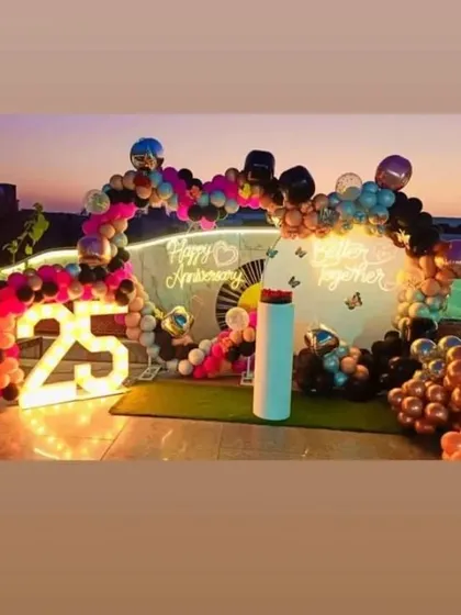 A colorful rooftop 25th-anniversary party at sunset. The setup includes a balloon arch, a 'Better Together' neon sign, and a large light-up number '25'.