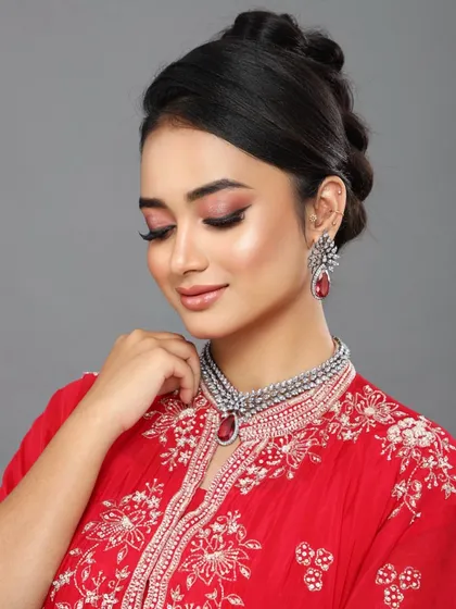 A close-up of a client in a vibrant red outfit, perfect for a festive event. The makeup is classic, with defined eyes and a neutral lip.