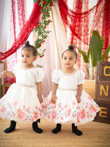Twin girls looking adorable in their matching floral dresses for their first birthday shoot. Capturing the sweetness of twins is a special joy.