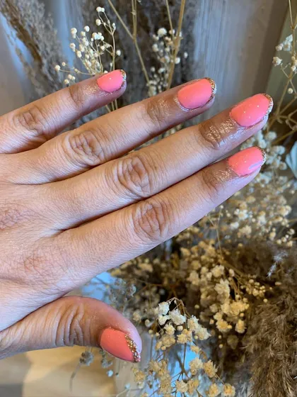 The perfect summer color. This manicure features a bright coral-pink polish with a delicate gold glitter line along the cuticle for a chic finish.