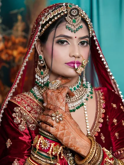 This student's bridal look features a rich velvet lehenga with striking green jewelry. The makeup complements the look with a bold lip and defined eyes.