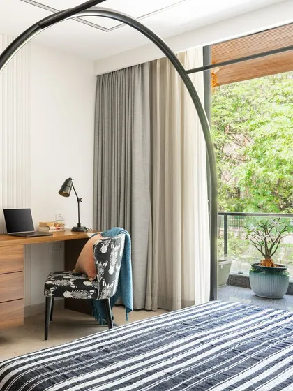 A functional workspace is seamlessly integrated into the bedroom design, overlooking a green balcony. The simple wooden desk and patterned chair provide a comfortable spot for work without disrupting the room's restful atmosphere.