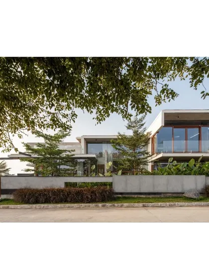 A view of The Quarry House framed by the foliage of a nearby tree. The design intentionally integrates with the landscape, with trees and plants playing a key role in the overall composition.