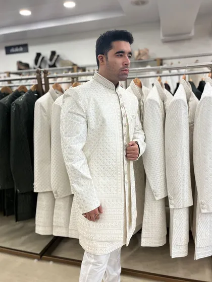 This client is checking the fit of our textured ivory sherwani. The clean lines and subtle self-design make it a sophisticated choice for any wedding event.