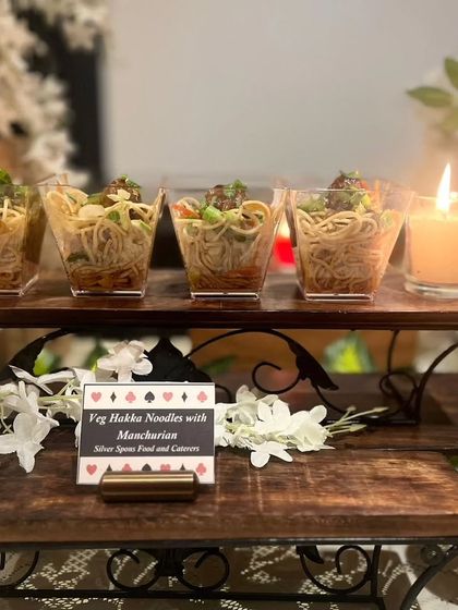 Individual portions of Veg Hakka Noodles with Manchurian, elegantly presented on a tiered stand. The candle-lit setting adds to the warm, festive atmosphere of the Diwali party.