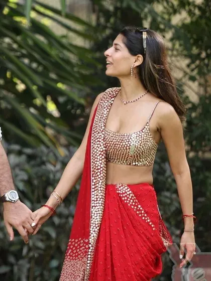 A candid shot of a bride in her stunning red and gold outfit, adorned with a delicate ruby and diamond necklace.