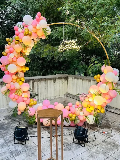 This circular ring backdrop is a popular choice for modern celebrations. Here, I've decorated it with a vibrant mix of pink, peach, and gold balloons and a "Happy Birthday" neon sign for a chic outdoor party on a terrace.