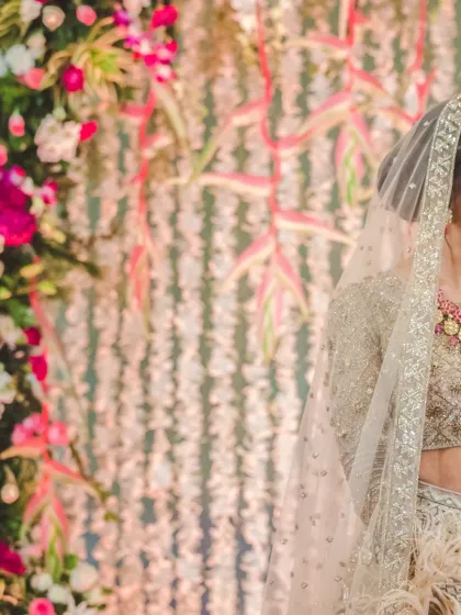 A candid side-profile of a smiling bride in a beautiful sequined lehenga, set against a backdrop of flowers.