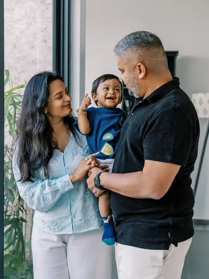 A happy family portrait taken indoors by a large window, celebrating their son's birthday with laughter and joy.