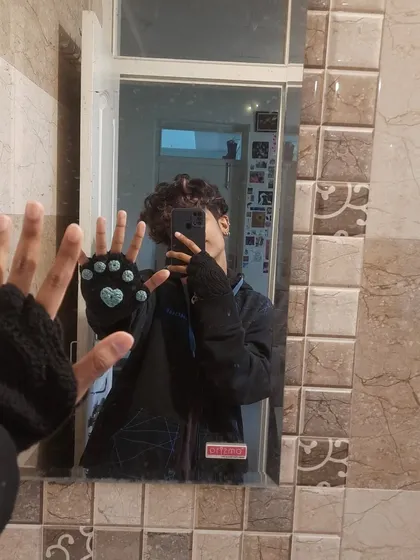 A mirror selfie showing off the crochet cat-paw gloves. They have little toe beans and a heart on the palm.