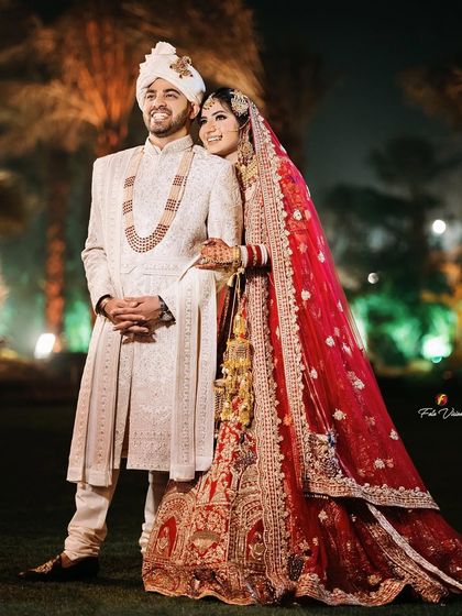 A classic wedding night portrait of the couple, her in a stunning red lehenga and him in an elegant white sherwani.