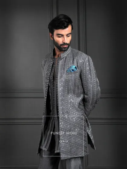 A charcoal grey kurta, woven with geometric lines and subtle shimmer. Finished with looped fabric buttons and a regal mandarin collar, it is a harmony of structure and elegance.