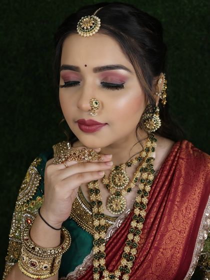 A detailed close-up of the jewellery and makeup paired with the red and green half-saree. The set includes multiple necklaces, jhumkas, and a maang tikka.