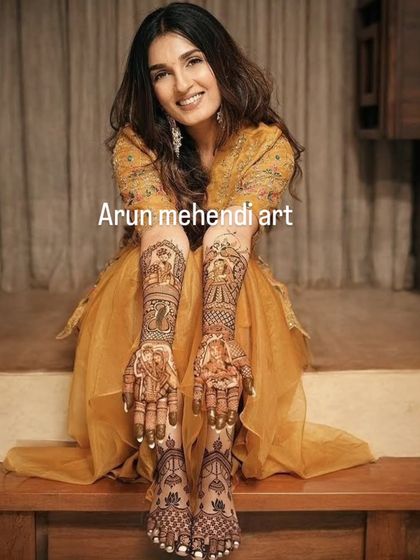 A happy bride showcasing her complete storybook mehendi. The design flows from her hands to her feet, filled with portraits and traditional wedding scenes.