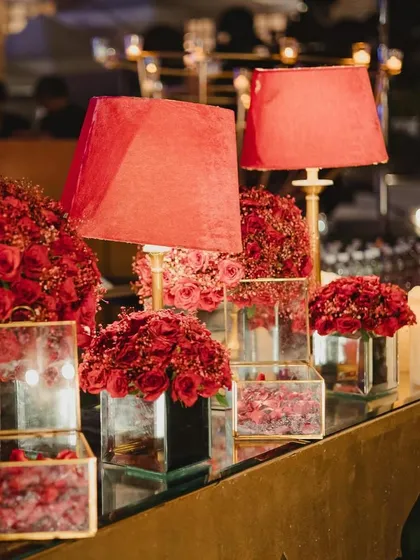 A lavish bar setup with deep red roses, lampshades, and candles, creating a romantic and opulent atmosphere.