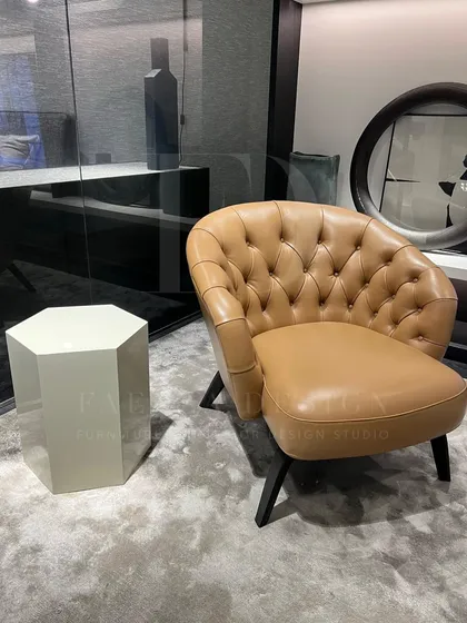 A classic tub chair upholstered in tan leather with deep button-tufting. This piece combines timeless design with luxurious material, perfect for a study or a sophisticated living room corner.