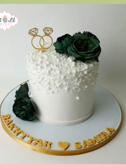 An elegant engagement cake for Bakhtiyar and Samira. The white pearl-textured cake is accented with deep green roses and a golden ring topper.