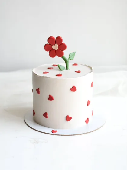 A sweet and simple cake decorated with tiny red hearts and topped with a single red fondant flower. This minimalist design is perfect for showing someone you care.