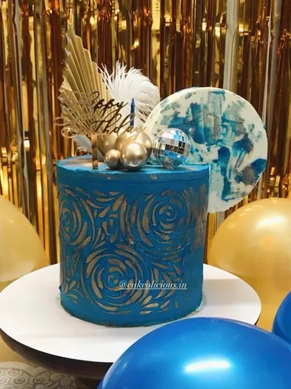 An asymmetrical cake I made for my brother's birthday. This modern design features a bold blue ganache with a gold stenciled pattern, topped with a disco ball, feathers, and an abstract chocolate sail.