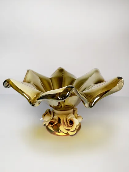 This Murano masterpiece captivates with its fluid, ruffled form, with each fold catching the light in a mesmerizing dance. Resting on a delicate rose-adorned base, it is a blend of artistry and grace.