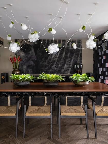 The 'Hybrid Table' in the Caitriona dining room, with its intricately carved base and solid wood top, sets the stage for stylish dining. Above, a Bocci installation with air plants adds a whimsical, organic touch.