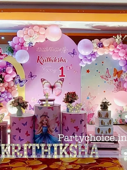 An elaborate butterfly theme for a first birthday celebration. This setup features a large balloon arch in pastel colors, multiple butterfly props, a light-up number '1', and a beautifully decorated cake display area.