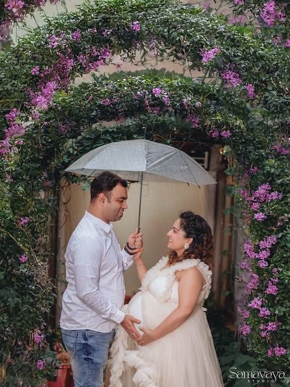 A romantic couple's portrait under an umbrella, surrounded by a beautiful floral arch. This shot proves that any weather can be perfect for a maternity shoot.