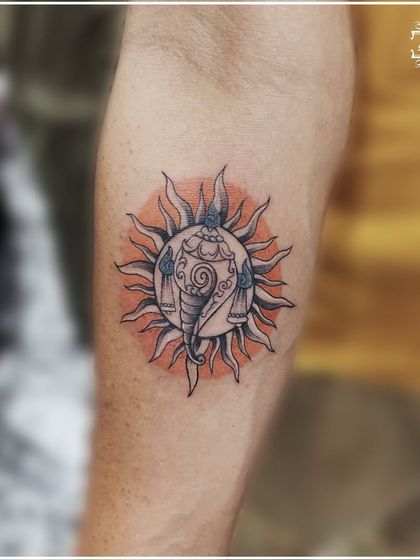 A unique tattoo of Ganesha within a sun mandala, representing the removal of obstacles and the dawning of new energy. The orange watercolor splash adds a beautiful warmth to the piece.