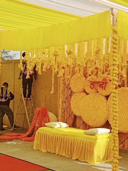 My team at work setting up an elaborate Haldi backdrop, carefully hanging strings of fresh yellow marigolds.