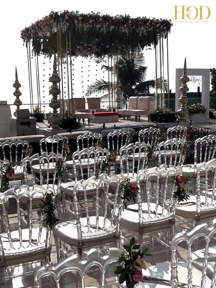 Another angle of the seaside mandap, highlighting the clear ghost chairs and the floral arrangements tied to them, ensuring every detail is perfect.