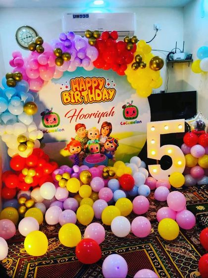 A Cocomelon party designed for a smaller space at home. The room is filled with colorful balloons on the floor and a vibrant arch over a personalized backdrop.