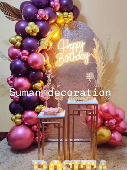 A stylish birthday setup with a purple and pink metallic balloon garland against a silver glitter backdrop. The look is completed with a neon sign and modern gold stands.