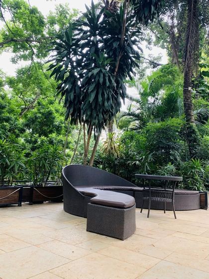 A modern and comfortable outdoor lounge seat placed in a patio area, surrounded by the lush greenery of our gardens. A perfect spot to relax.