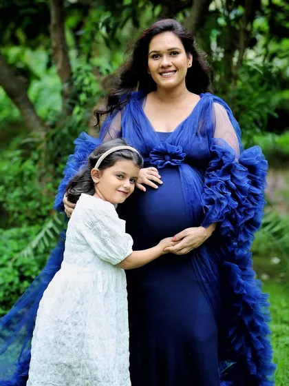 A lovely outdoor portrait of a mother and daughter. The daughter gently holds her mom's hand on the baby bump, sharing in the excitement of the new arrival amidst a beautiful garden setting.