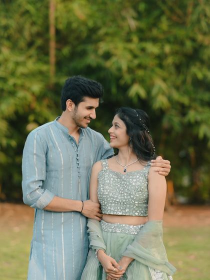 A sweet portrait of a couple looking at each other with loving smiles. The natural green background complements their elegant attire and highlights their connection.