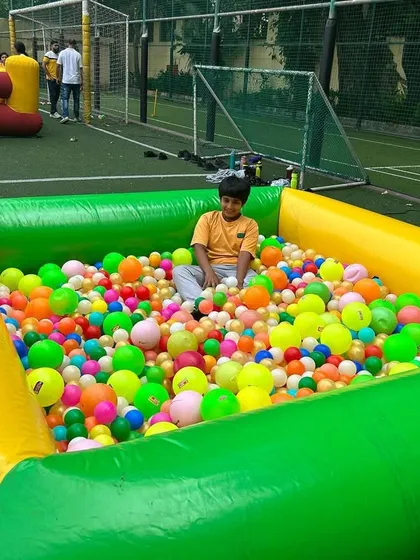 A large inflatable ball pit filled with colorful balls, set up outdoors on a turf lawn. It is big enough for several kids to play in safely.