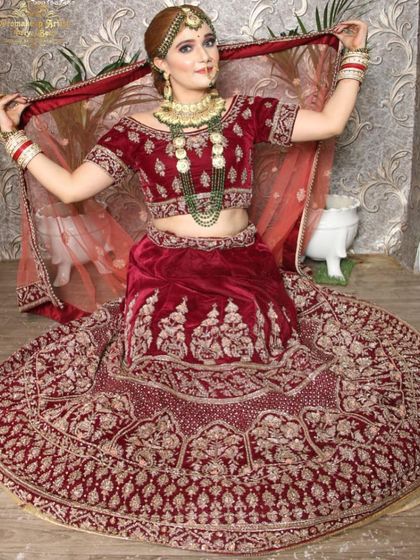 This off-shoulder velvet maroon lehenga offers a modern twist on a classic bridal look. Paired with a layered green beaded necklace, it creates a unique and fashionable statement.