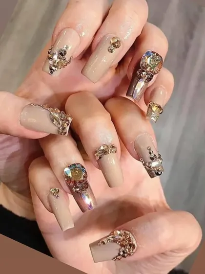 The definition of luxury. These long, square-shaped nails feature a nude base and are heavily adorned with an array of gold and iridescent rhinestones in various shapes and sizes for a truly decadent look.