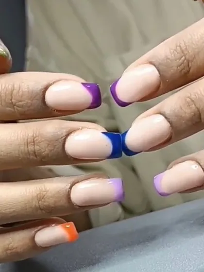 A close-up of a multi-colored French manicure, showcasing a variety of bold colors on the tips of square nails.