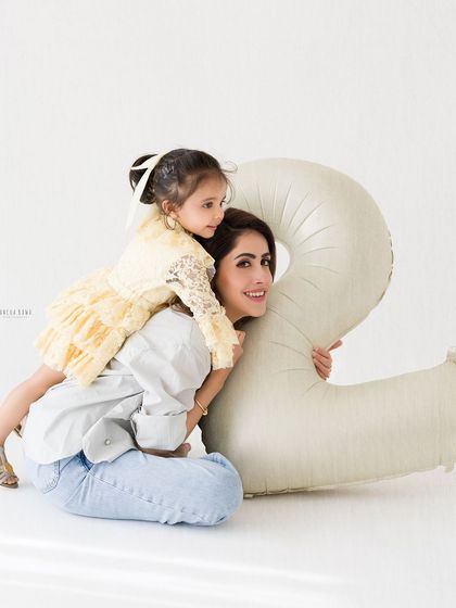 A mother and daughter share a sweet moment during a milestone photoshoot. The daughter lies playfully on her mother's back.