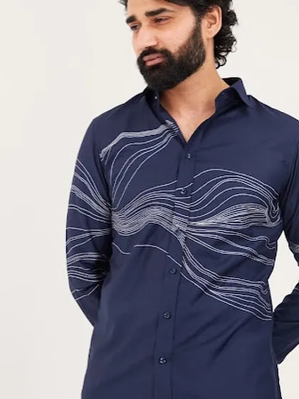 This navy blue shirt features abstract wave-like embroidery in white thread that flows across the chest and sleeve. The design is dynamic and modern, inspired by natural forms.