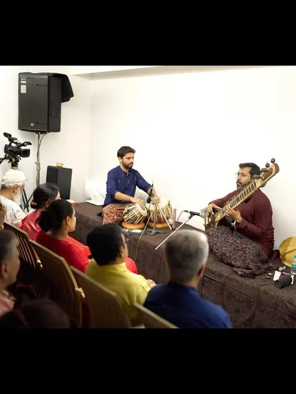 A wider view of the house concert, showing the audience deeply engaged in the sitar and tabla performance.