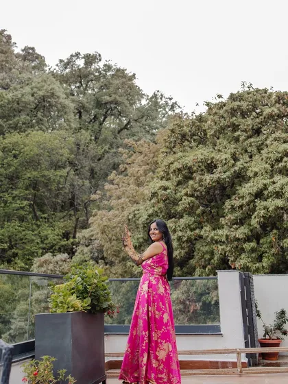 A full-length shot of the bride showing off her Mehendi, posing happily on a balcony with a backdrop of dense green trees.