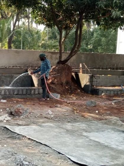 A worker watering newly constructed planter boxes at the cathedral site, ensuring the concrete cures properly before backfilling with soil.