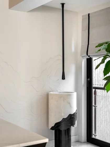 A detail shot in the Evelyn project, featuring a custom pedestal washbasin with waveform details that echo the textures used elsewhere in the home. The ceiling-suspended faucet adds a sleek, modern touch.