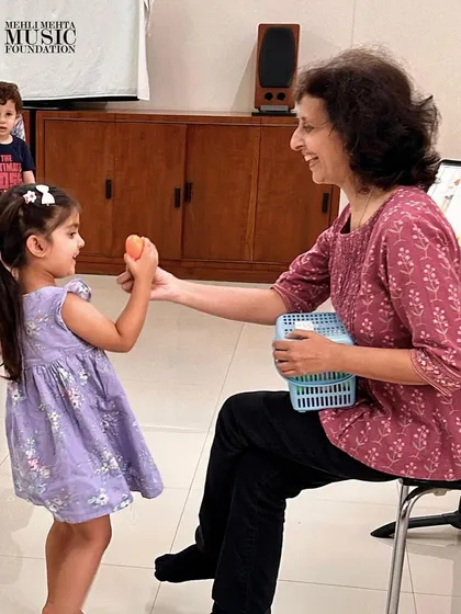 A teacher shares a shaker with a young student, encouraging her to explore sound and rhythm. These one-on-one interactions are key to building a child's confidence.