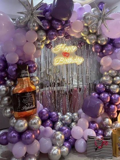 Yeh 40th birthday setup ka close-up hai. Isme purple aur silver chrome balloons ke saath ek "Aged to Perfection" whiskey bottle foil balloon bhi hai.
